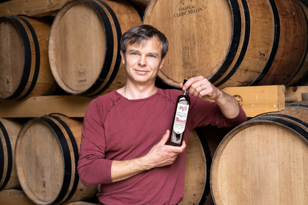 Benoit Badin devant tonneaux de vinaigre présentant son vinaigre de vin rouge